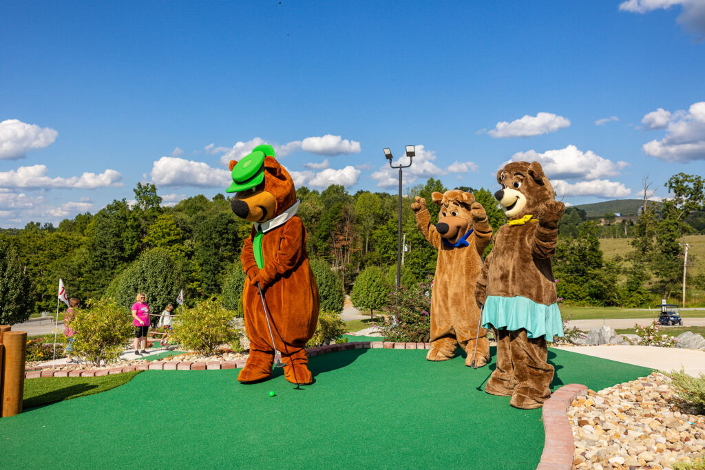 Yogi Bear Playing Mini Golf | Jellystone Park™ Mill Run Yogi Bear lines up a putt while Boo Boo and Cindy Bear cheer him on at the Mini Golf course at Jellystone Park™ Mill Run in Pennsylvania.