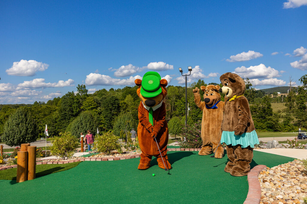 Yogi Bear Putting on the Mini Golf Course | Jellystone Park™ Mill Run Yogi Bear putting on the mini golf course while Boo Boo and Cindy Bear watch at Jellystone Park™ Mill Run in Pennsylvania.